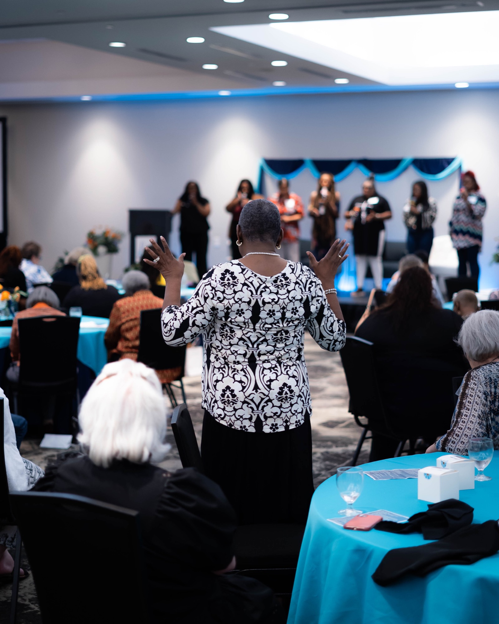 Women raising hands in worship at a past Be1 Experience gathering